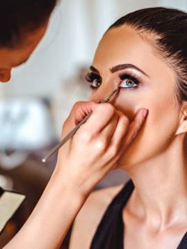 a woman applying eyeliner pencil on another woman