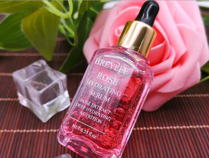 bottle of serum with eyedropper laying beside a real pink rose